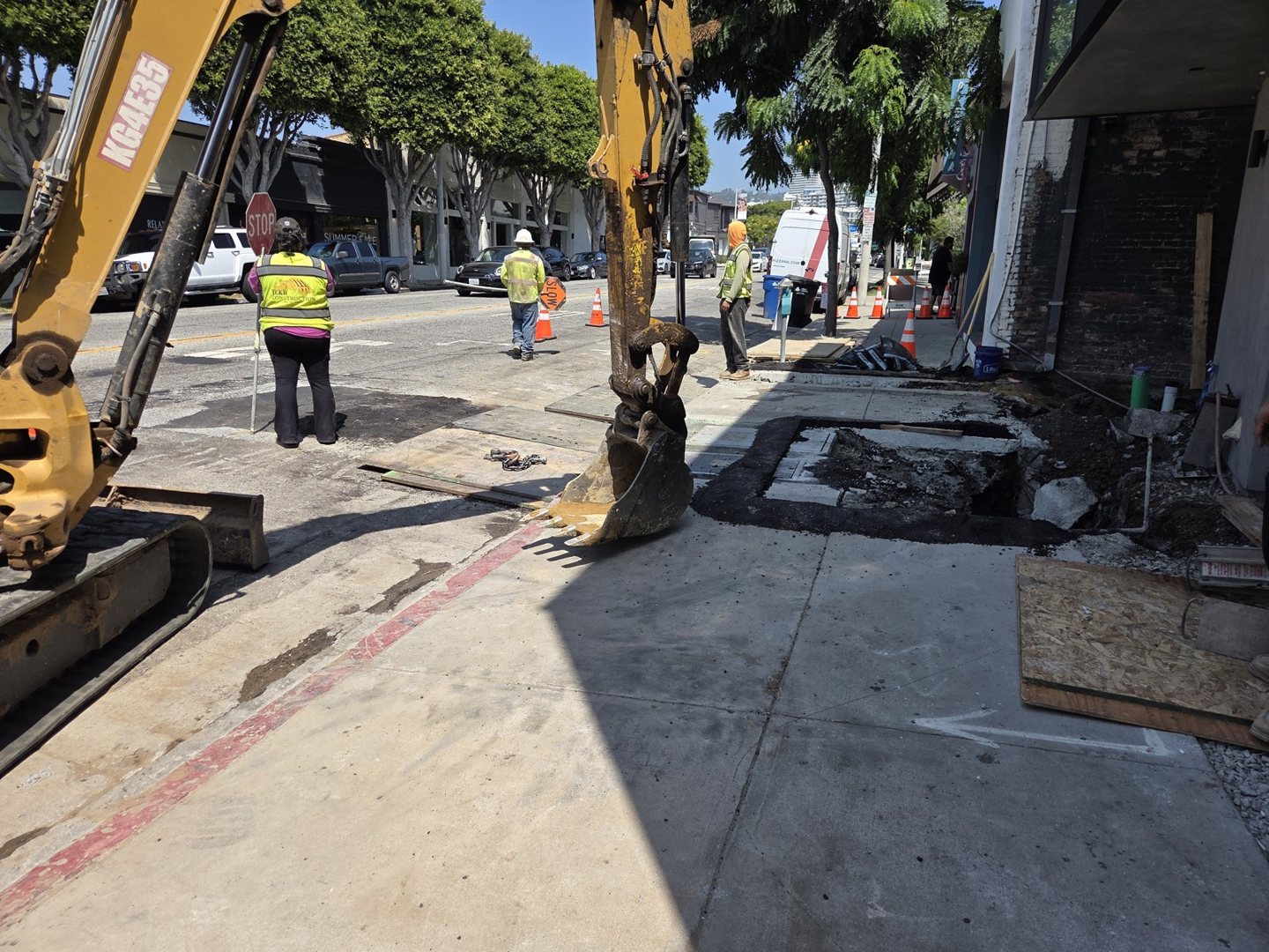 Excavator and workers beside the curb and sidewalk at the Robertson Boulevard project frontage.
