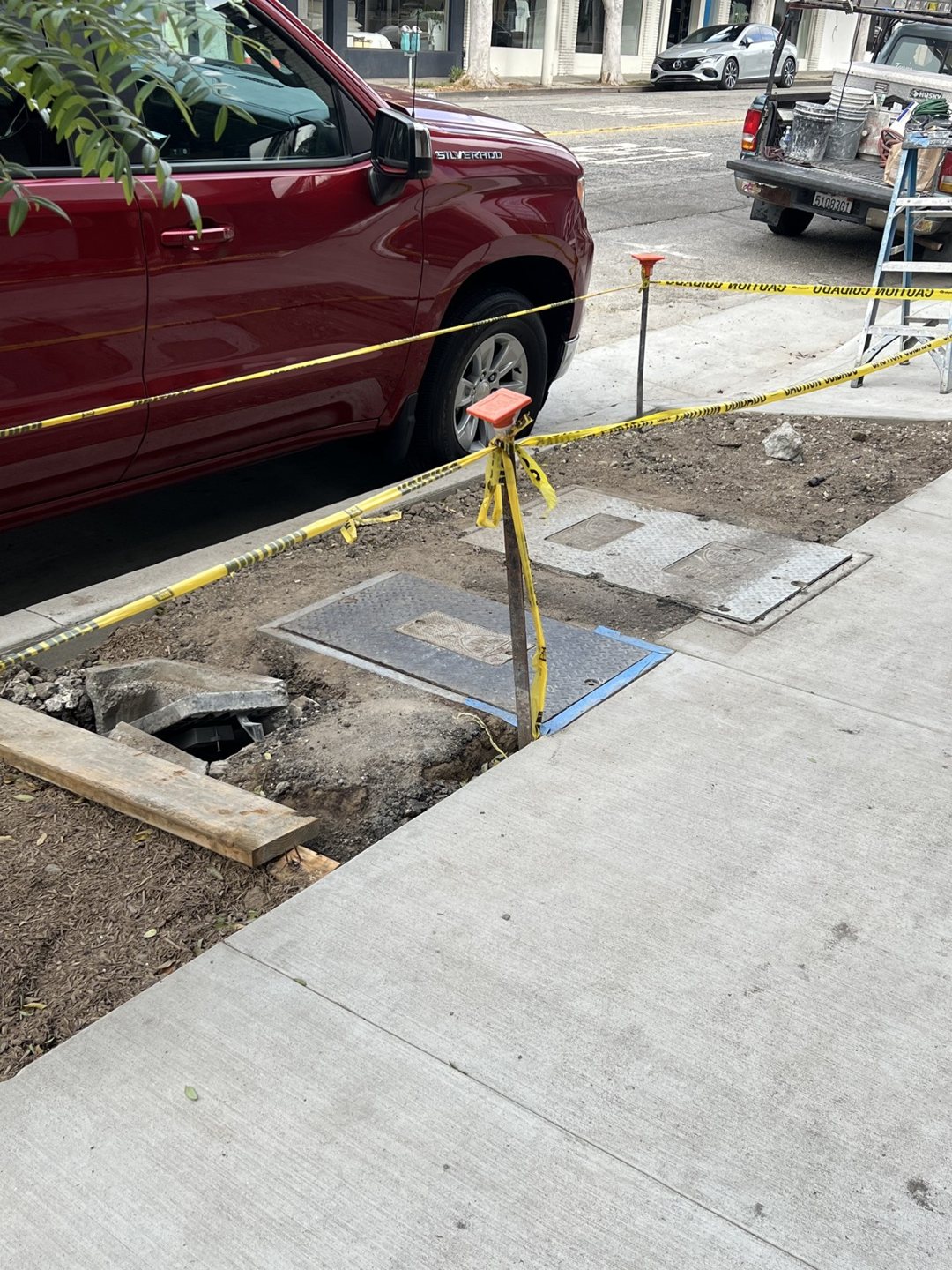 Meter covers and open work areas beside the sidewalk, marked with caution tape.